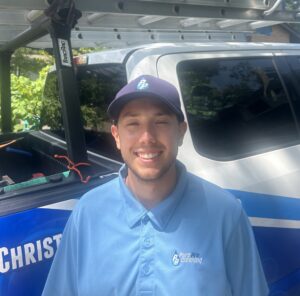 A man in a blue Pyro Pro Cleaning uniform and hat stands in front of a company vehicle with cleaning equipment and holiday lights, ready for professional holiday light installation services.